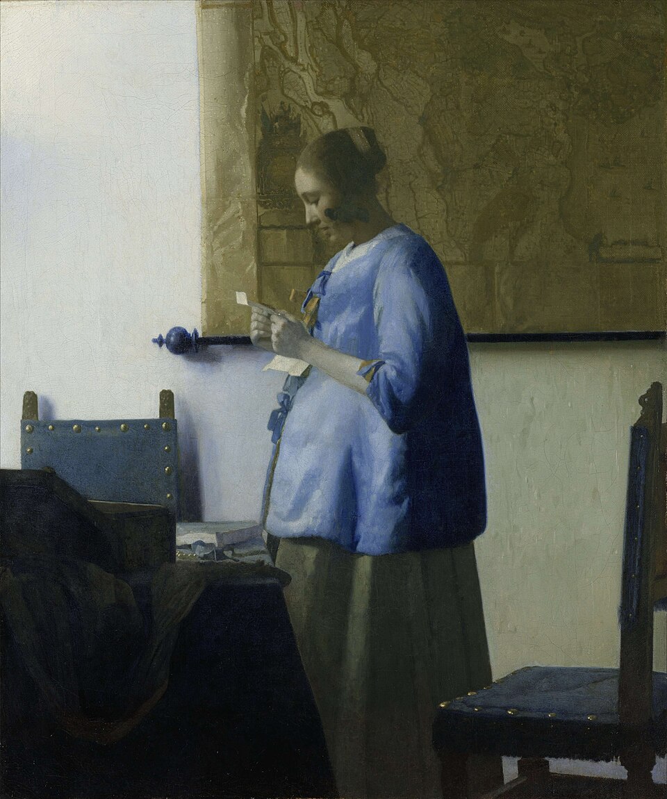 Johannes Vermeer’s Woman in Blue Reading a Letter: a woman in a blue jacket stands in soft window light, absorbed in a letter held in both hands.