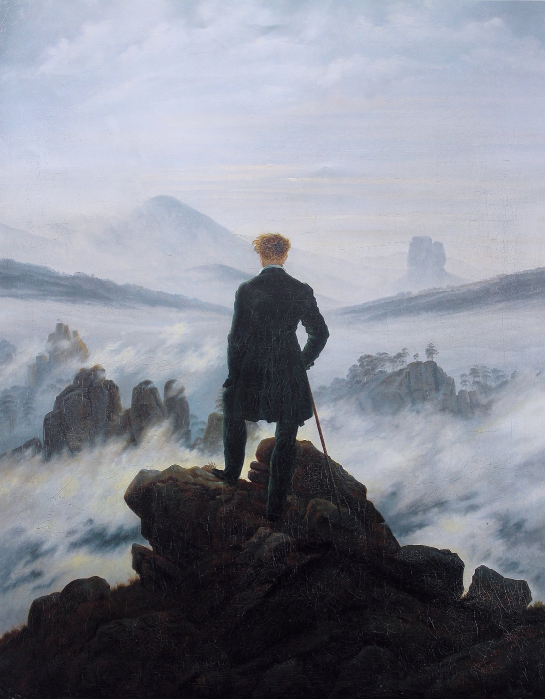 Caspar David Friedrich’s Wanderer above the Sea of Fog: a man in a dark green coat, seen from behind, stands on a rocky summit with a walking stick, looking out over a sea of fog broken by rocky peaks and distant mountains.
