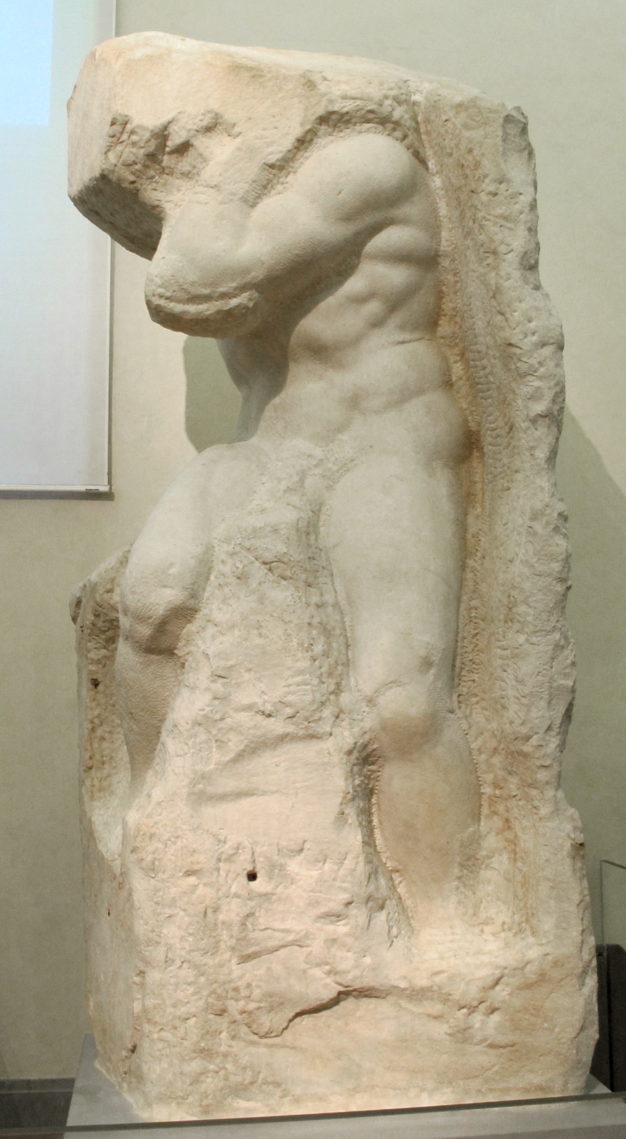 An unfinished marble Slave by Michelangelo: a muscular torso and legs pushing out of a rough block, the head still buried in uncut stone.